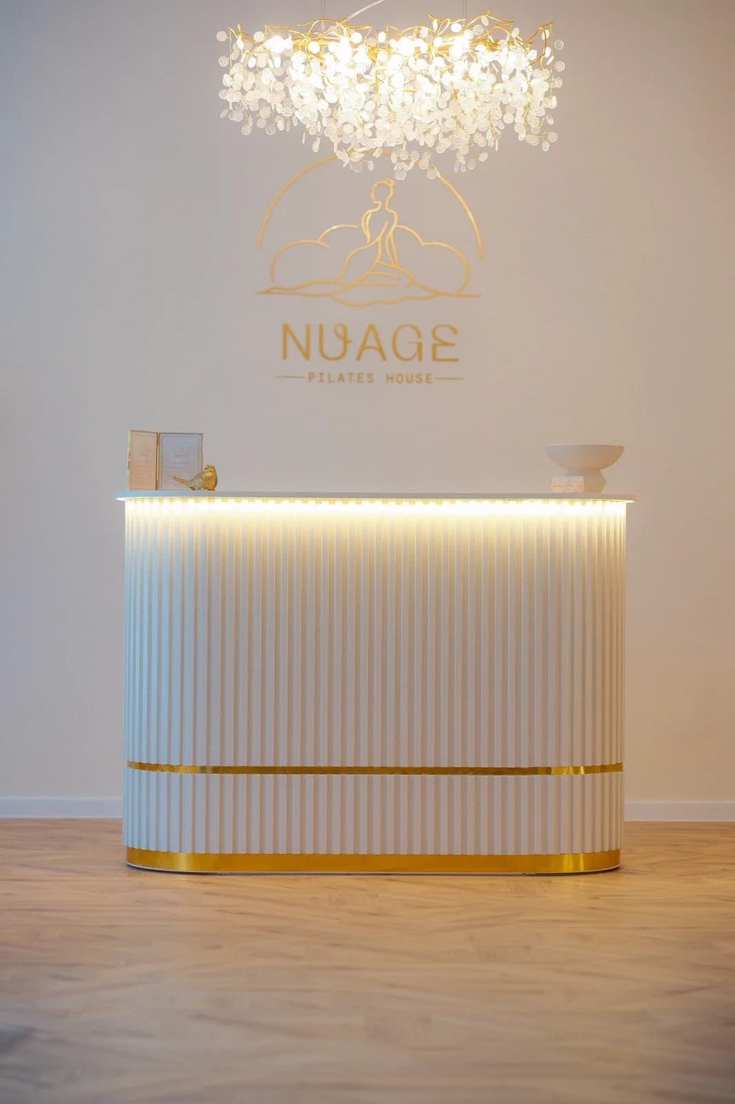 Рецепцията на NUAGE Pilates House със златен детайл и логото на стената